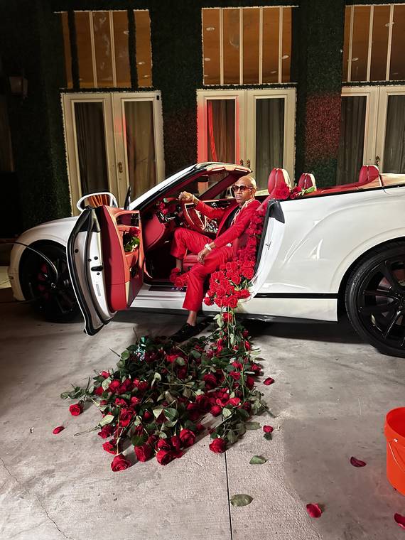 Benzo Trill in a red suit in a white convertible filled with roses, from the Roses music video